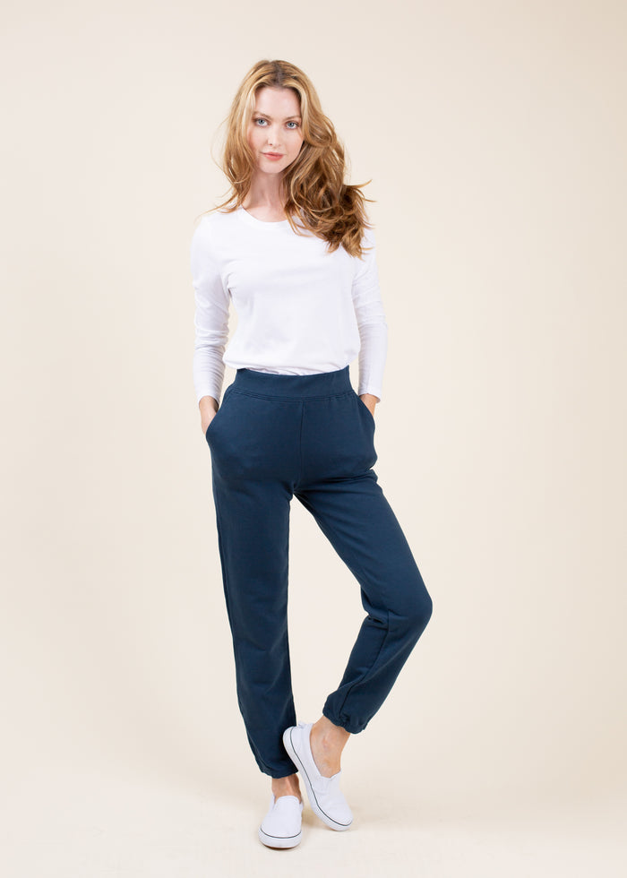 Woman wearing a white long-sleeve top and navy jogger on a beige background