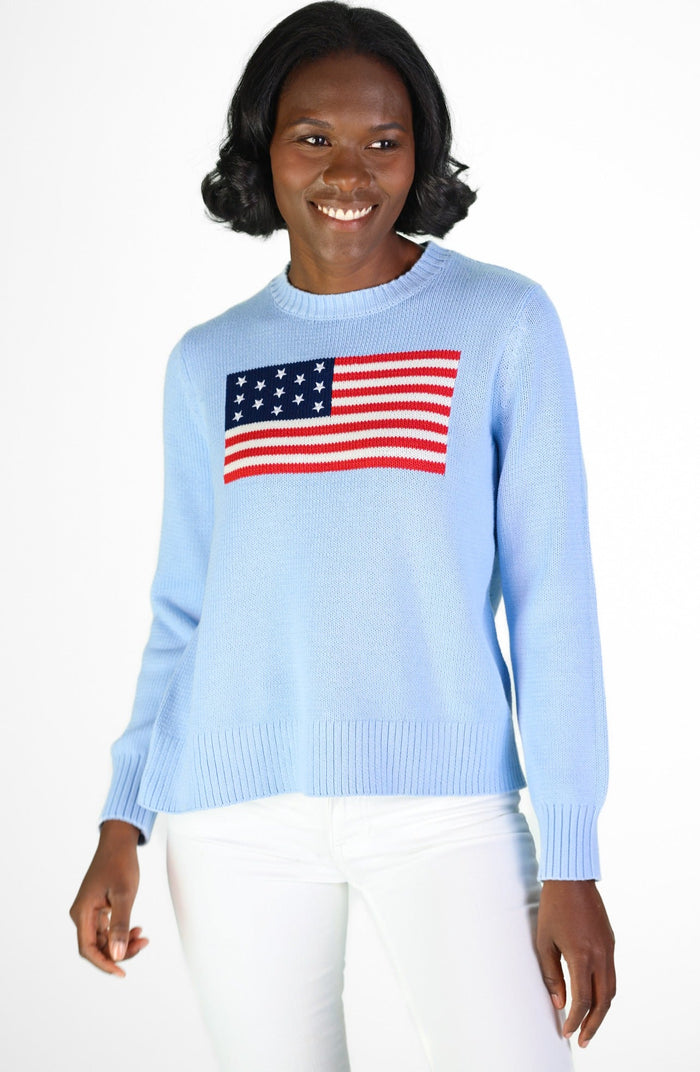 Smiling model in a light blue sweater with American flag, paired with white pants