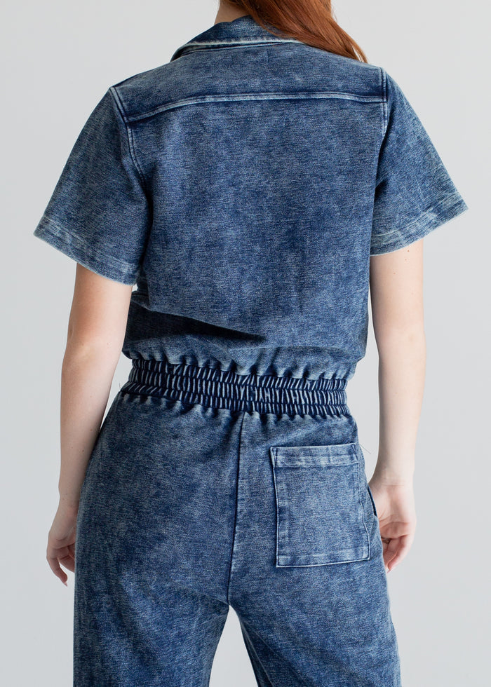Person wearing a blue denim jumpsuit on a plain background