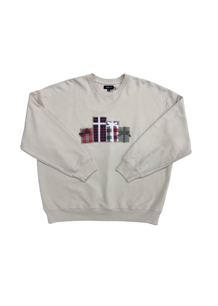 A light beige crewneck sweatshirt featuring a colorful graphic of stacked gift boxes with plaid patterns on the chest, displayed flat against a white background.