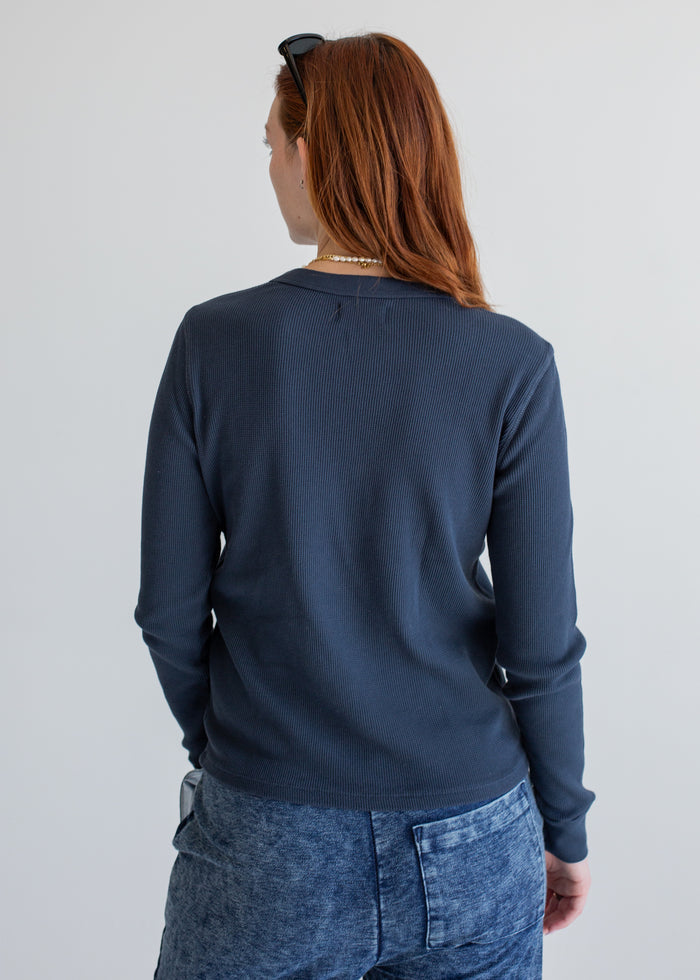 Person wearing a navy blue long sleeve and jeans on a plain background
