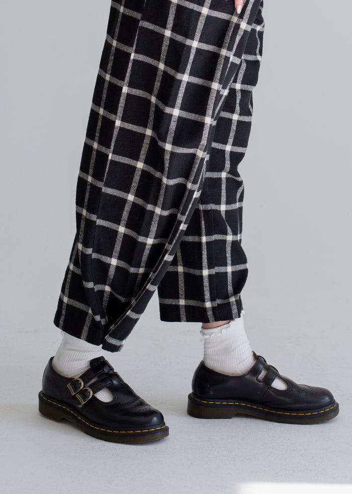 Person wearing black checkered pants and black shoes on a plain background