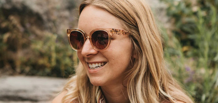A pair of rose-colored sunglasses with a paisley pattern being worn, with a natural green background.