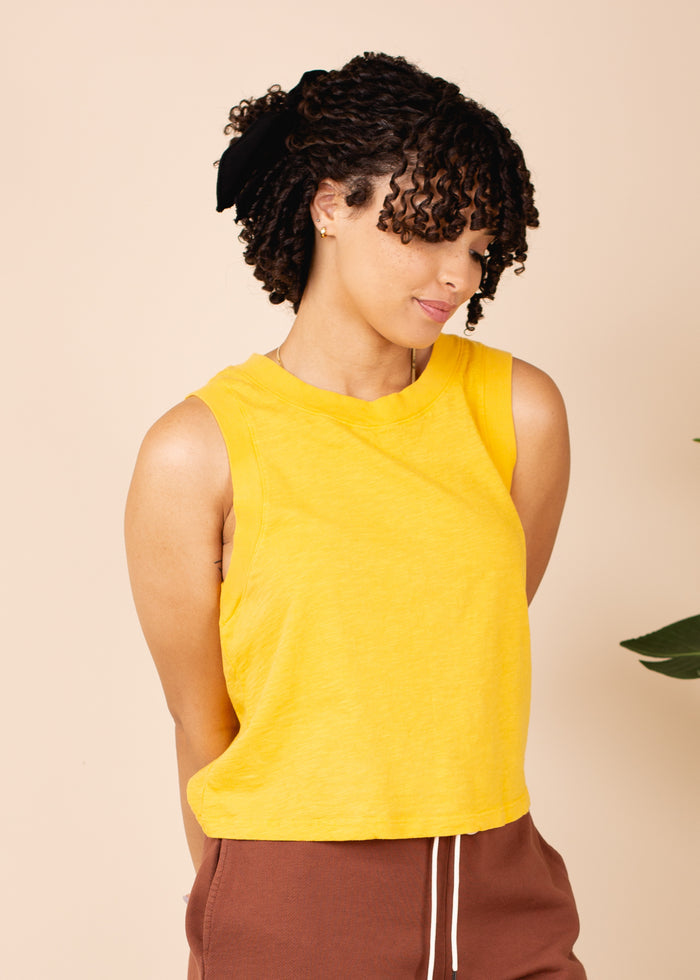 Woman wearing a yellow sleeveless top against a beige background