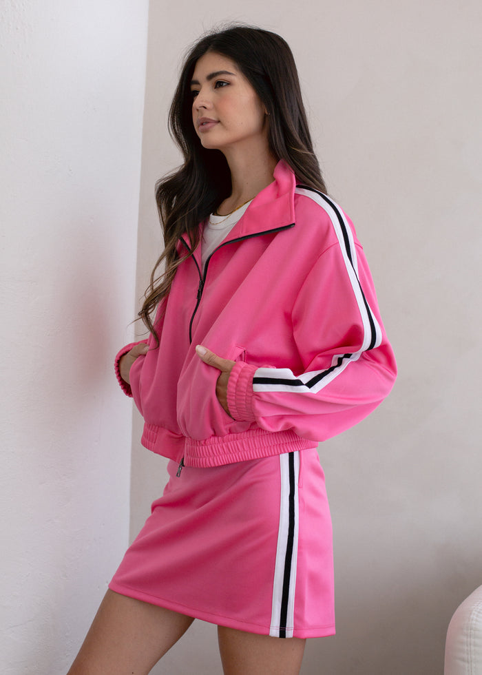 Woman wearing a pink tracksuit with white stripes on a plain background