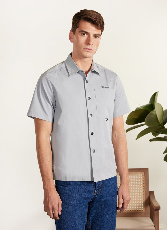 A model wears the Percival Auxiliary Boxy Clerk Shirt in light blue, a short sleeve style with snap buttons and embroidery.
