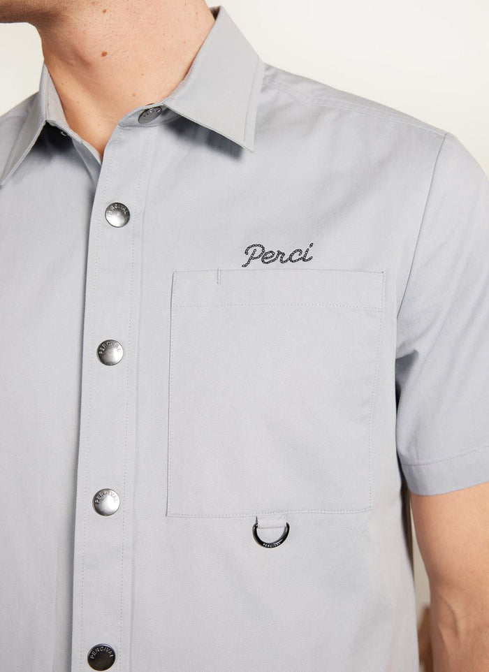Close up of the Percival Auxiliary Boxy Clerk Shirt in light blue, showing the embroidery, pocket, and snap button details.