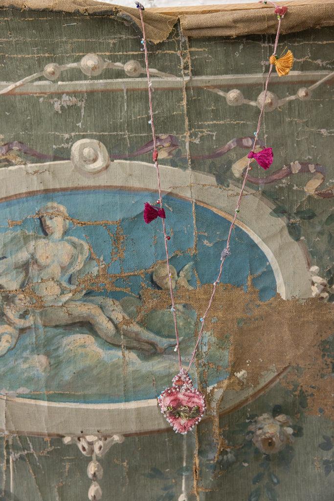 Magnolia Pearl artisan pink heart necklace with whimsical tassels, vintage painted backdrop