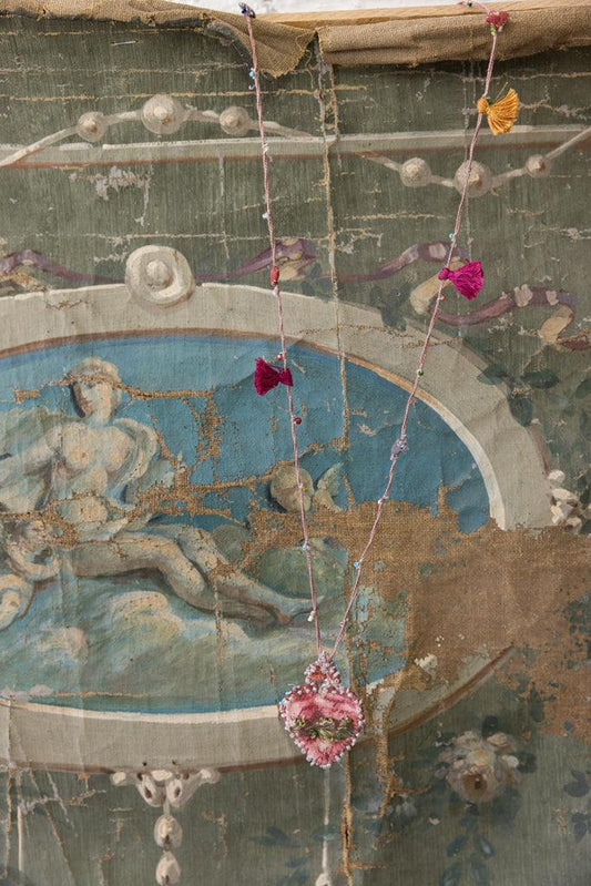 Magnolia Pearl artisan pink heart necklace with whimsical tassels, vintage painted backdrop