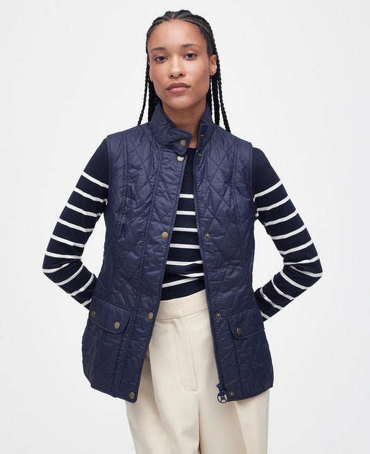 Woman wearing a navy quilted vest over a striped shirt with a white background