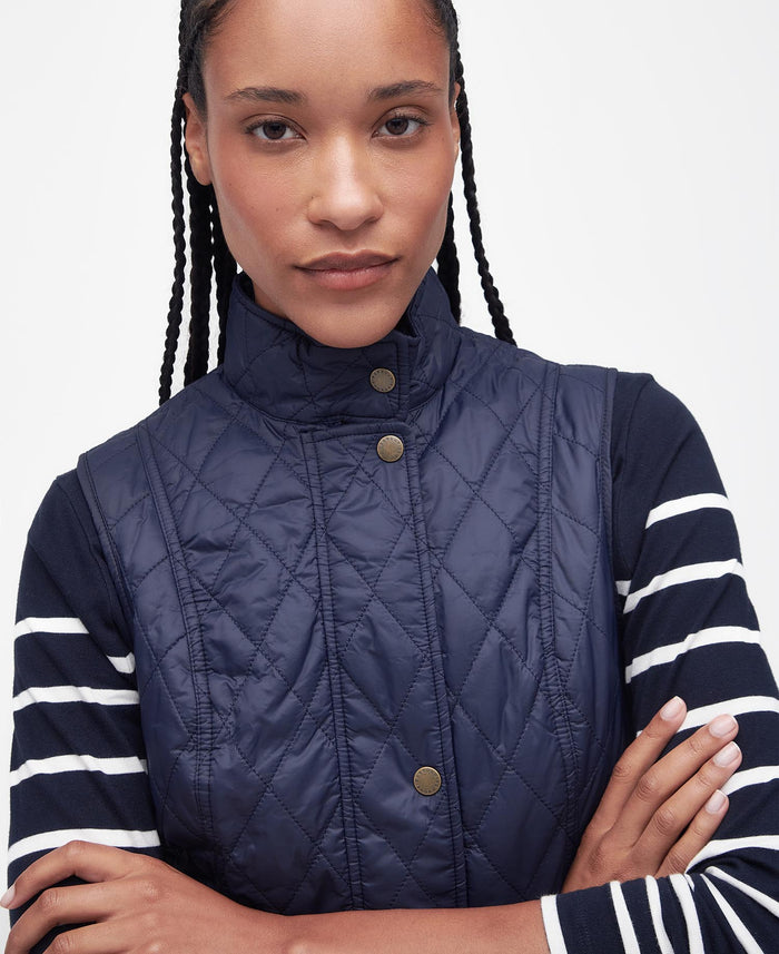 Person wearing a navy quilted vest over a striped shirt with a plain background