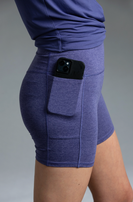 Person wearing Indigo shorts with a pocket holding a phone on a gray background || Indigo