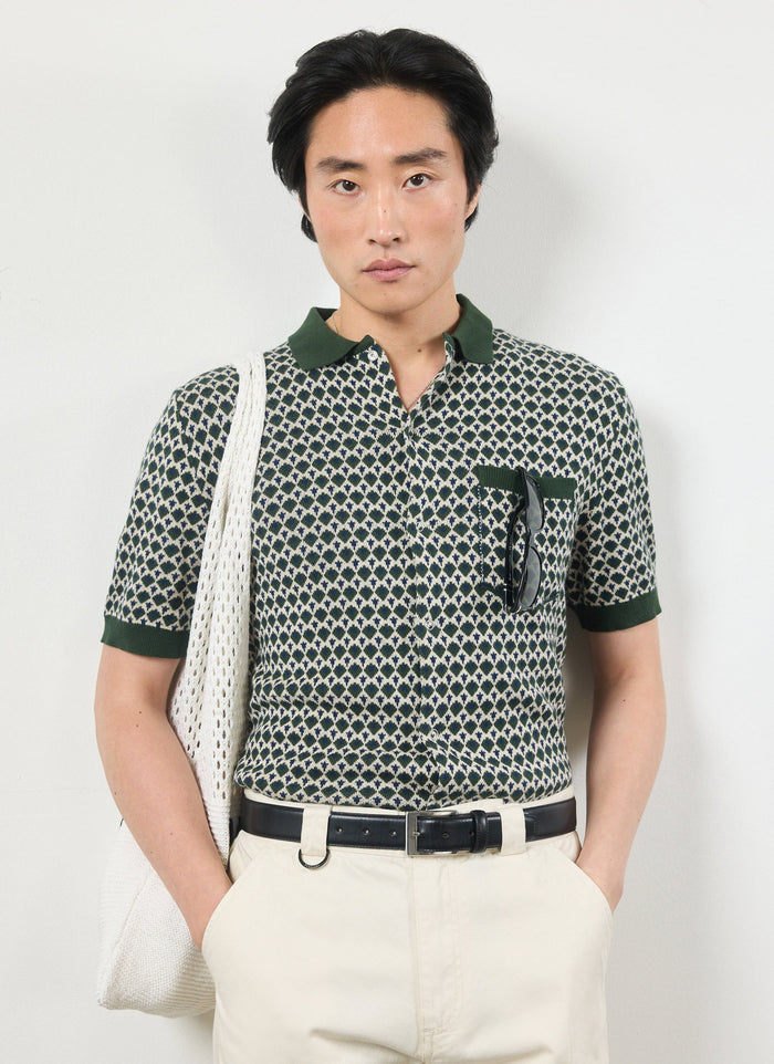 A model wears the Percival Casa Piccante knitted shirt in green jacquard, styled with cream trousers and a white tote bag.