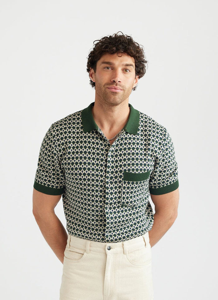 A man models the Percival Casa Piccante knitted shirt in green and cream jacquard, styled with off-white trousers.