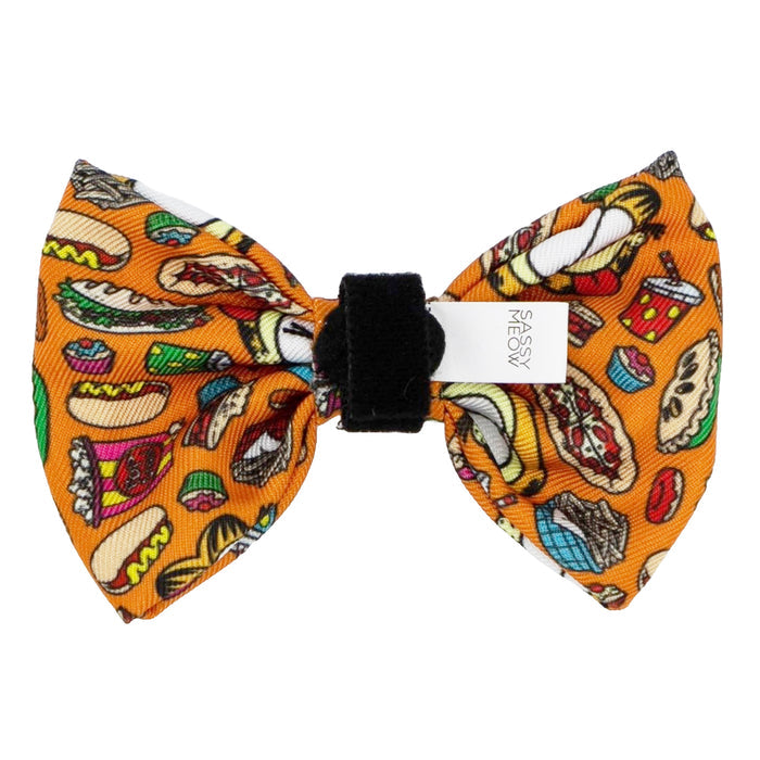 The Cat Bowtie - Garfield™ by Sassy Woof is a food-themed orange bow tie with comics-style burgers, hot dogs, pizza, tacos, and drinks plus a white Sassy Meow tag—ideal for any Garfield cat collar.