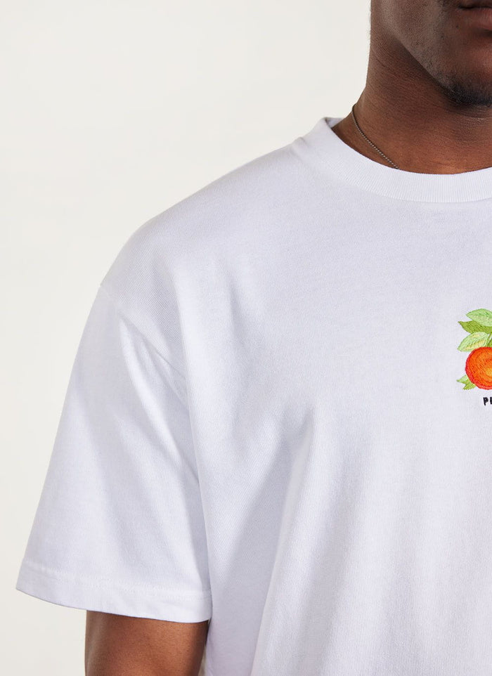 Close up of a model wearing the Percival white Citrus oversized t-shirt with its embroidered orange graphic.