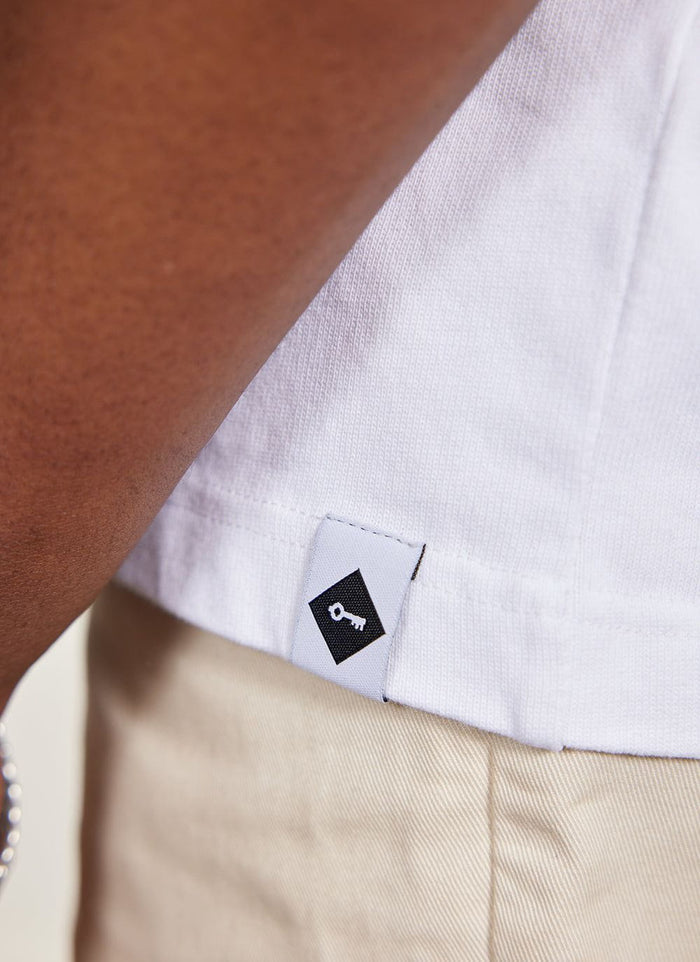Close up of the Percival key logo tab on the hem of the white Citrus oversized t-shirt.