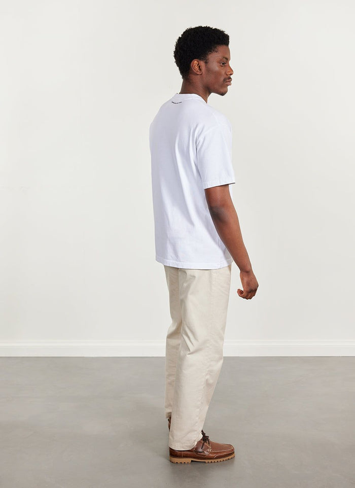 Side profile of a model wearing the Percival Citrus oversized t-shirt in white with cream trousers.