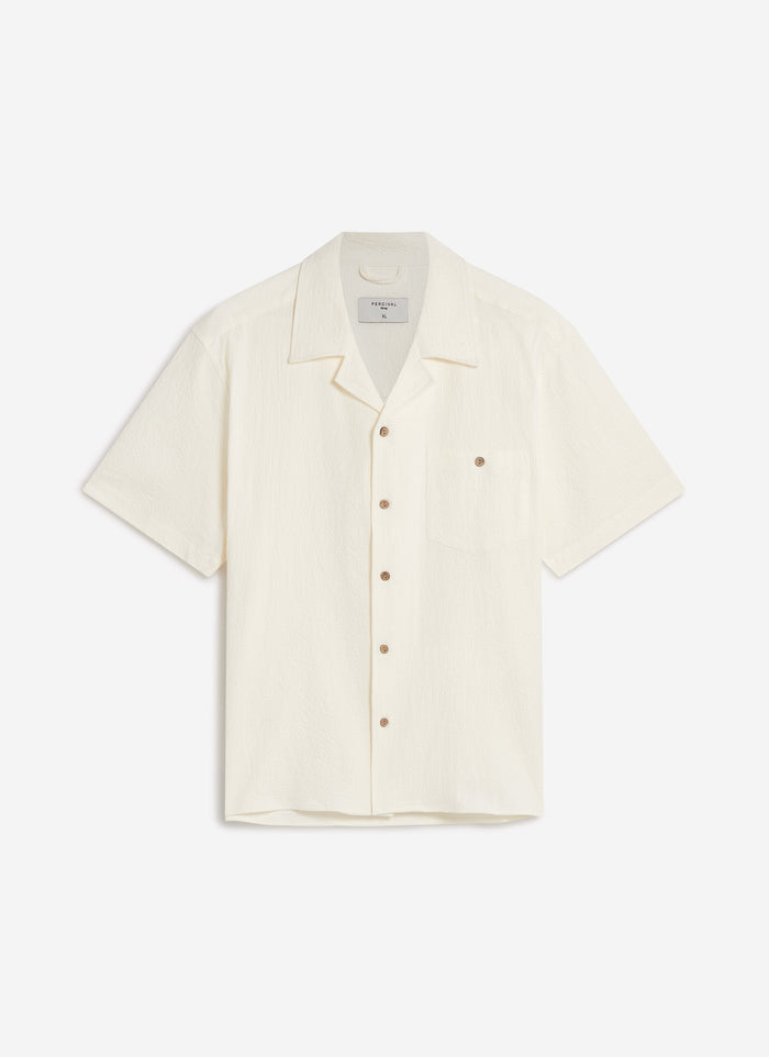 A flat lay of the Percival Cuban Shirt in ecru seersucker, showing the textured fabric, Cuban collar and chest pocket.
