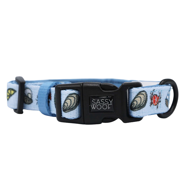 The Sassy Woof Dog Collar – Coastal Cuties features light blue fabric with seashell and ladybug designs, a black clasp, and D-ring—ideal for fans of coastal dog accessories.