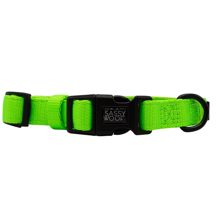 The Sassy Woof Dog Collar - Neon Green features a soft neoprene lining, adjustable fit, black plastic buckle with branding, and a sturdy black metal D-ring for leash attachment.