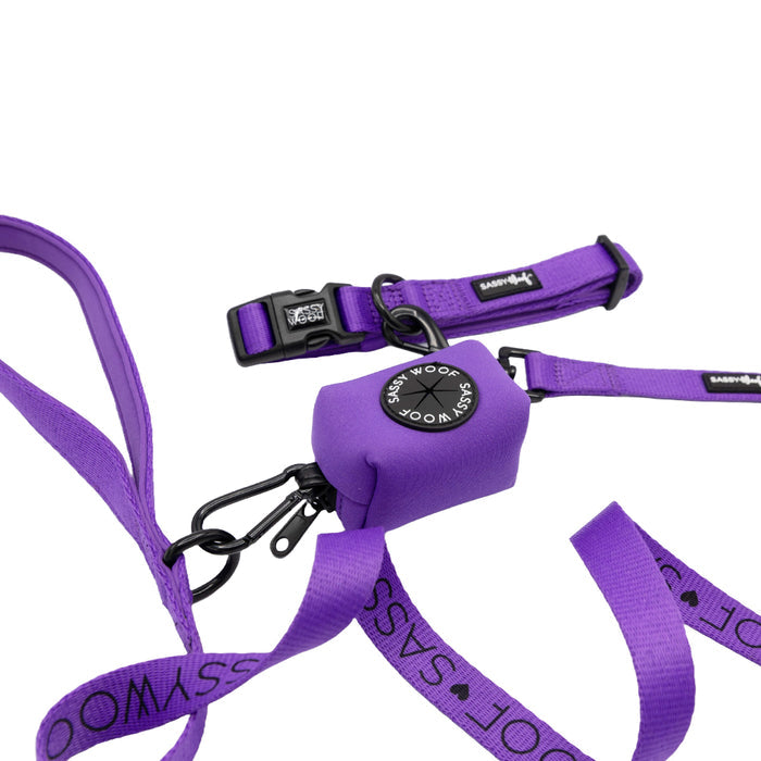 Introducing the Dog Collar Three Piece Bundle - Neon Purple by Sassy Woof: This vibrant set includes a neon purple dog leash and collar, both featuring black hardware, plus a matching poop bag holder. The leash is accented with the Sassy Woof logo repeatedly along its length in white text, making these eye-catching neon purple accessories both stylish and functional for your pup.