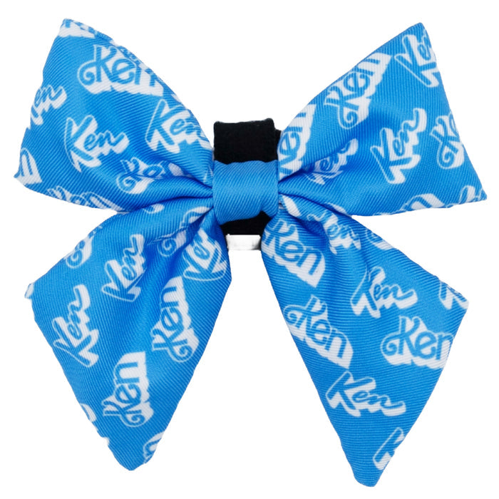 The Dog Sailor Bow - KEN™ by Sassy Woof is a blue bow tie with white Ken logos, gathered at the center with a black band and features adjustable Velcro straps for a secure fit.