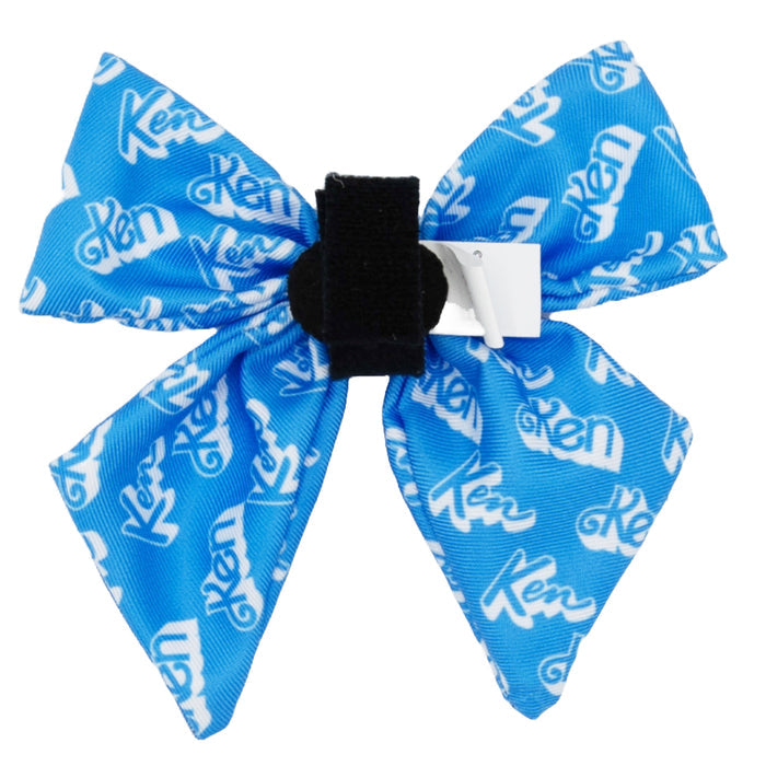The Dog Sailor Bow - KEN™ by Sassy Woof is a blue fabric bow with "Ken" printed in white, attached to an adjustable harness with Velcro straps, and finished with a black band and white tag.