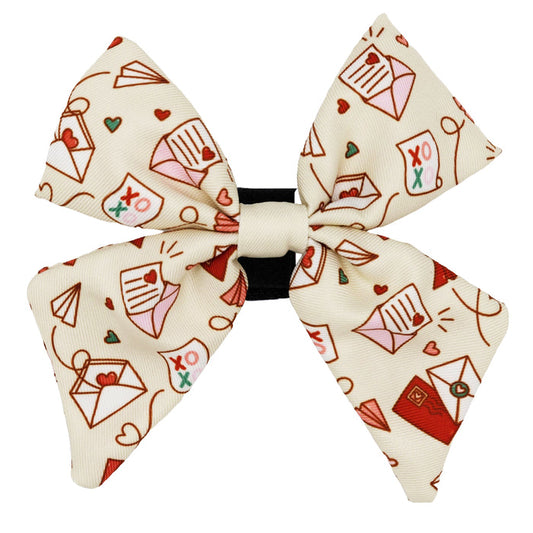 The Sassy Woof Dog Sailor Bow - P.S. I Woof You features a cream base with red, pink, and brown love letters, hearts, and envelopes on a black hair elastic—perfect for pups in need of heartfelt accessories.