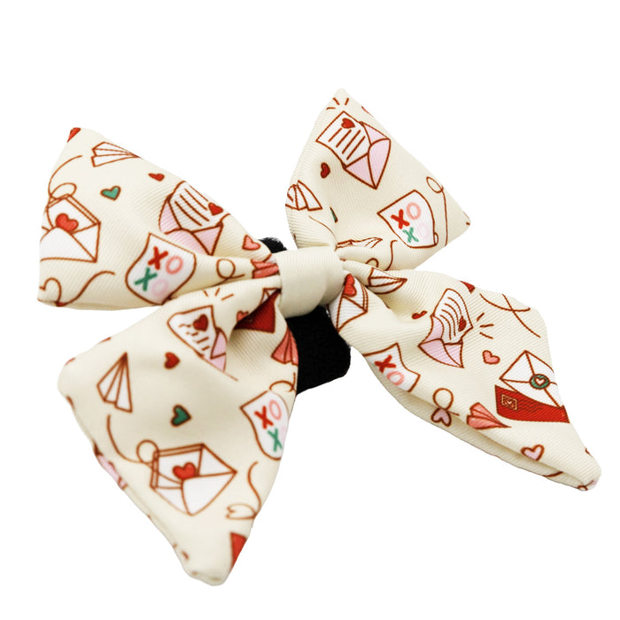 The Sassy Woof “Dog Sailor Bow - P.S. I Woof You” is a cream bow with red hearts, envelopes, and paper airplanes, plus XO and love letter motifs, finished with a black center band—perfect to pair with other Heartfelt Dog Accessories.