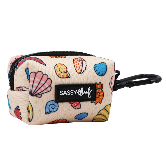 The Sassy Woof Dog Waste Bag Holder - Shell Yeah is a small beige pouch with colorful shell designs, a black zipper, and a clip—ideal as a beachy leash accessory or stylish waste bag holder for dog walks.