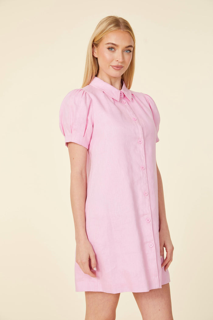 Smiling model in a mini pink linen dress, with a shirt collar, buttons down the front, and short puff sleeves