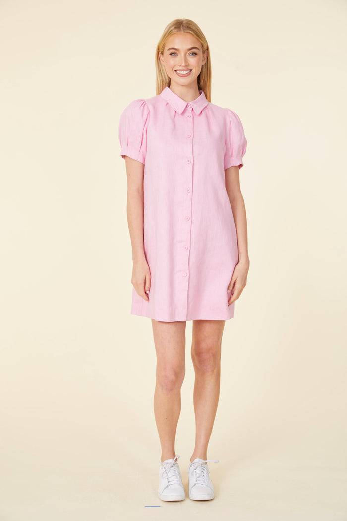 Smiling model in a mini pink linen dress, with a shirt collar, buttons down the front, and short puff sleeves