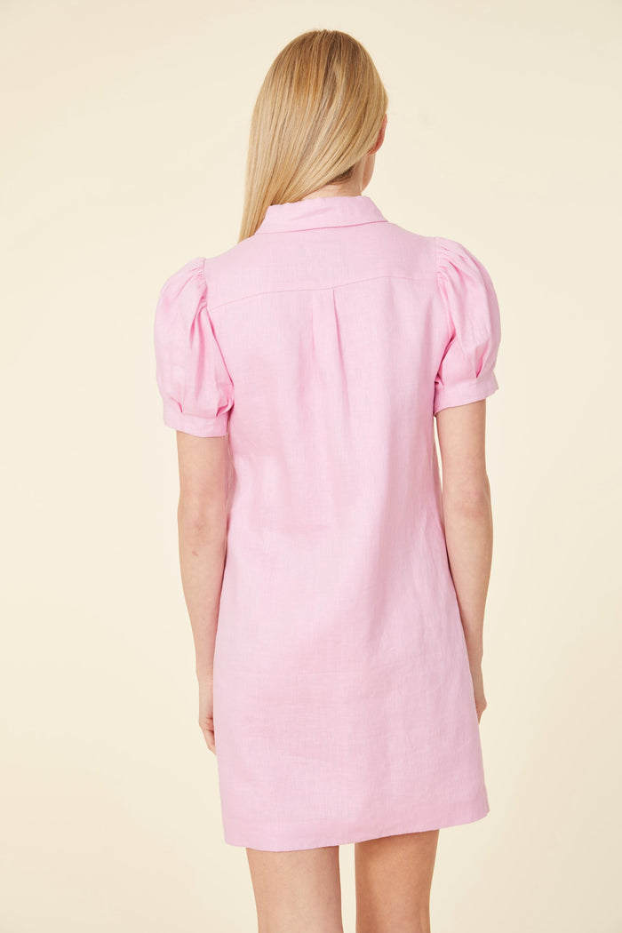 Smiling model in a mini pink linen dress, with a shirt collar, buttons down the front, and short puff sleeves