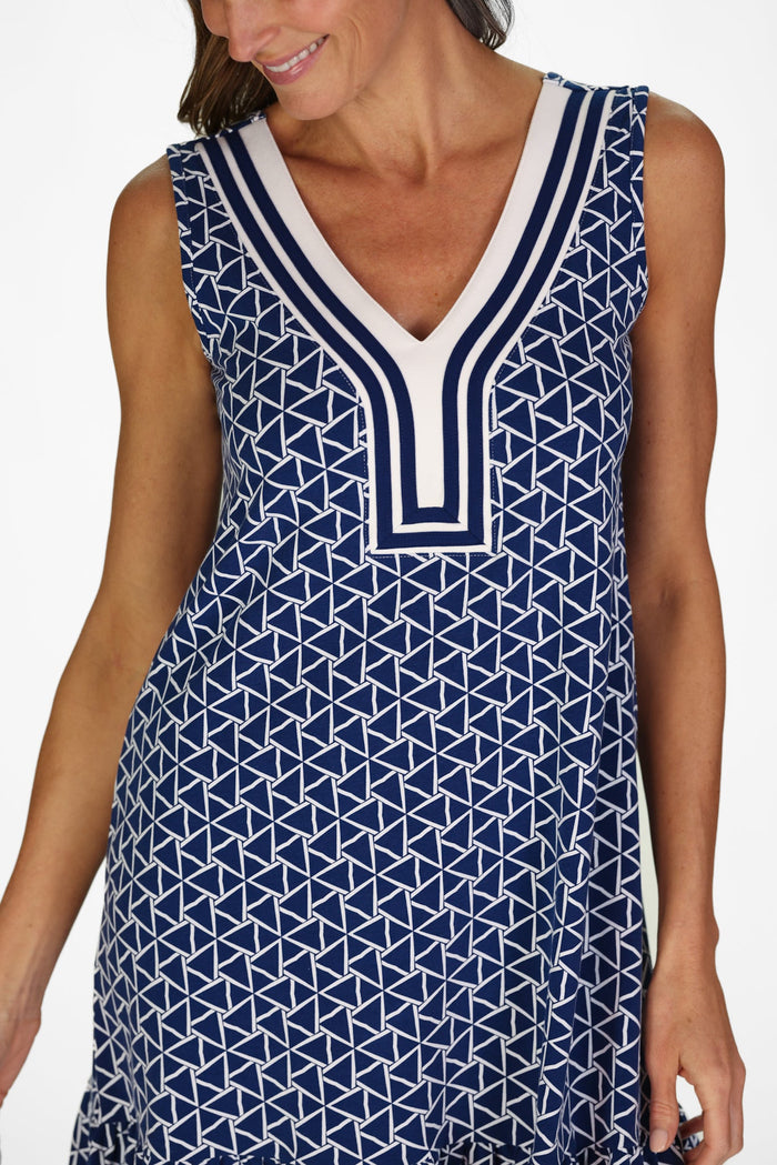 Woman wearing a sleeveless navy dress with a white geometric triangle pattern, deep V neckline with striped trim, and a flounced hem.