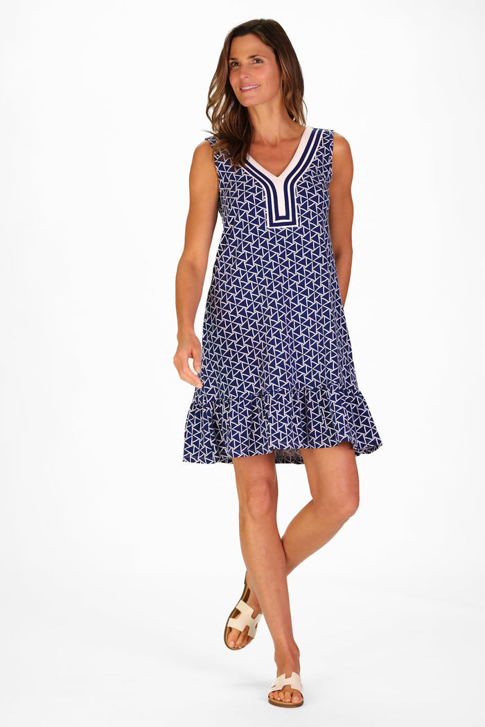 Woman wearing a sleeveless navy dress with a white geometric triangle pattern, deep V neckline with striped trim, and a flounced hem.