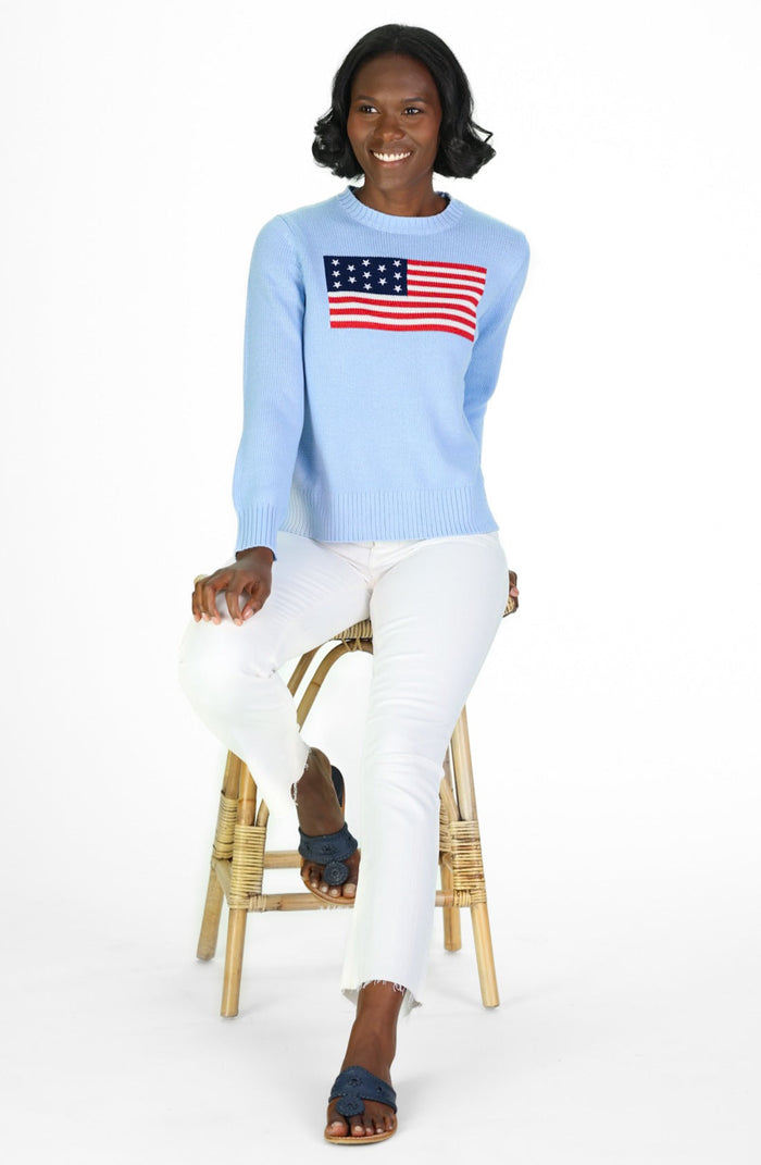 Smiling model in a light blue sweater with American flag, paired with white pants