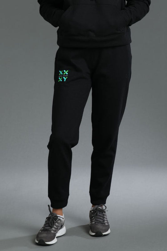 Person wearing black tracksuit with green logo on gray background || Black