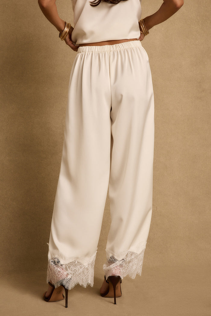 Back view of cream satin wide-leg pants with lace trim hem, worn with heels.