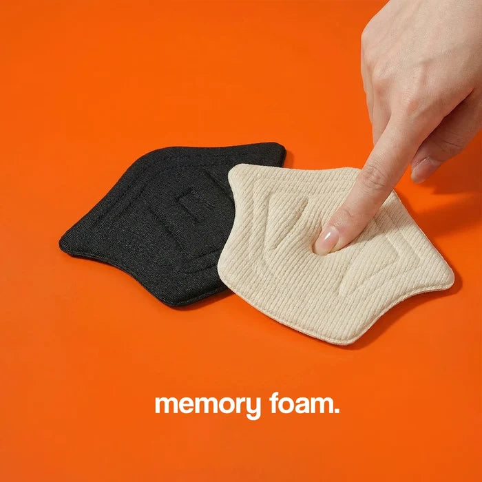 Heel cushion pads in black and beige memory foam, with a textured surface, placed on an orange background.