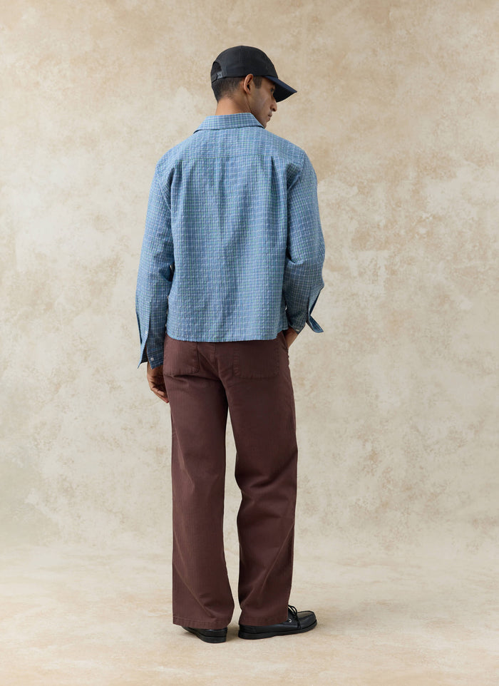 Rear view of the blue cotton Percival Hinsley Checked Boxy Shirt styled with espresso brown herringbone trousers.