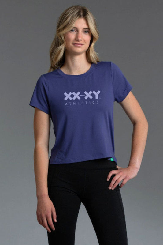 Woman wearing a blue 'XXXY Athletics' t-shirt on a gray background || Indigo