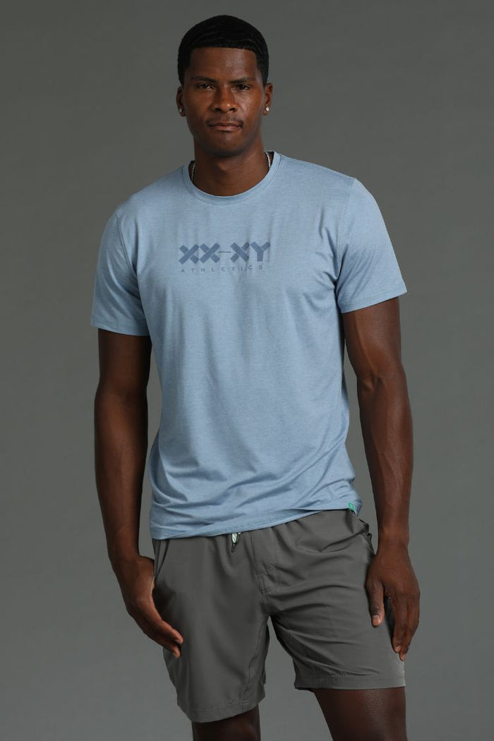 Man wearing a light blue t-shirt with a xx-xy logo and gray shorts || Cerulean Blue Heather