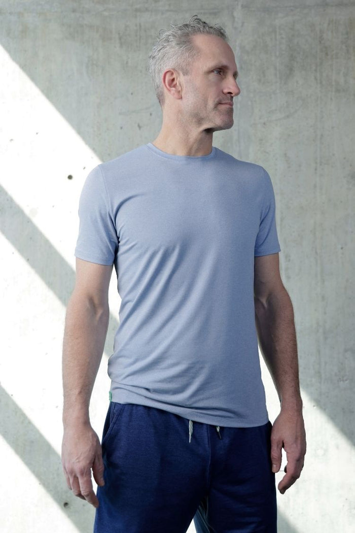 Man wearing a light blue t-shirt and dark blue shorts against a concrete wall. || cerulean blue heather
