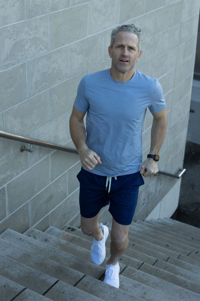Man running up a set of stairs wearing a blue t-shirt and navy shorts. || cerulean blue heather