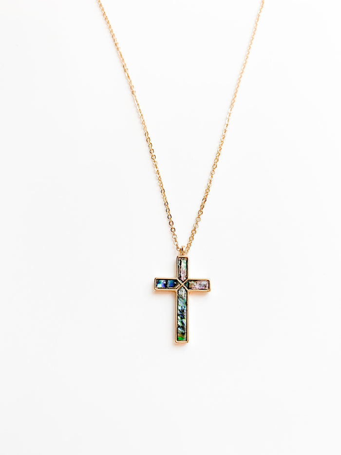Delicate gold necklace featuring a cross pendant with luminous abalone shell inlay, displaying natural ocean-inspired hues of blue, green, and pearl.