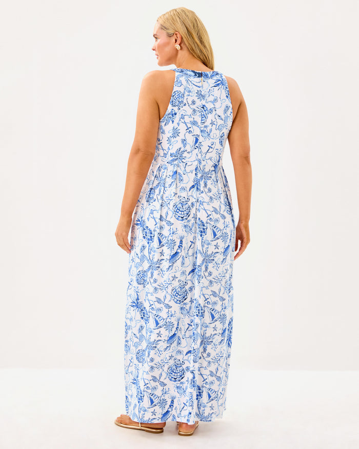Back view of model in the Lilly Pulitzer Carmilla Maxi Dress - Resort White - Barefoot Beachcomber. A sleeveless maxi dress with navy detailing around the collar and down the front, with blue beach motifs on a white background