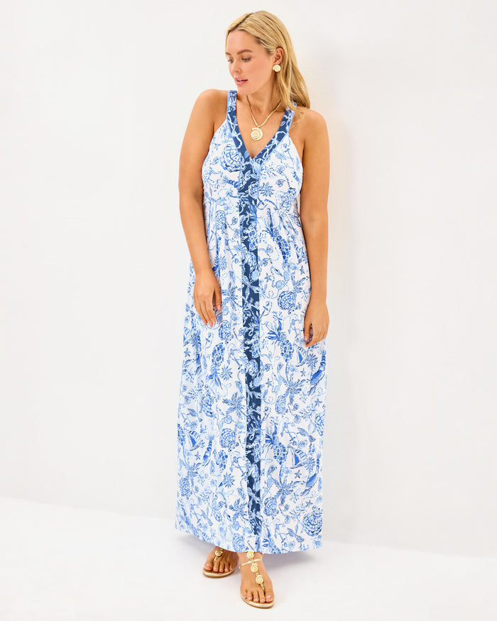 Full view of model in the Lilly Pulitzer Carmilla Maxi Dress - Resort White - Barefoot Beachcomber. A sleeveless maxi dress with navy detailing around the collar and down the front, with blue beach motifs on a white background