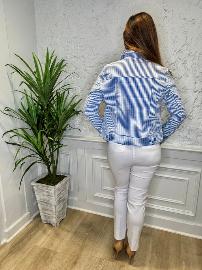 Smiling model in front of a white wall with a green plant in the corner. She's wearing the Lulu B Linen Travel Jacket - Seersucker, a light linen jacket with 2 front pockets and lightly frayed hems. Paired with a white shirt and white pants.