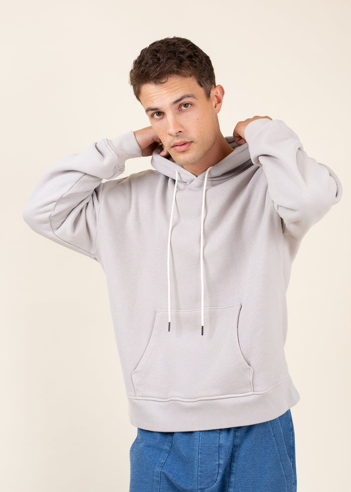 Man wearing a light gray hoodie and blue pants on a beige background